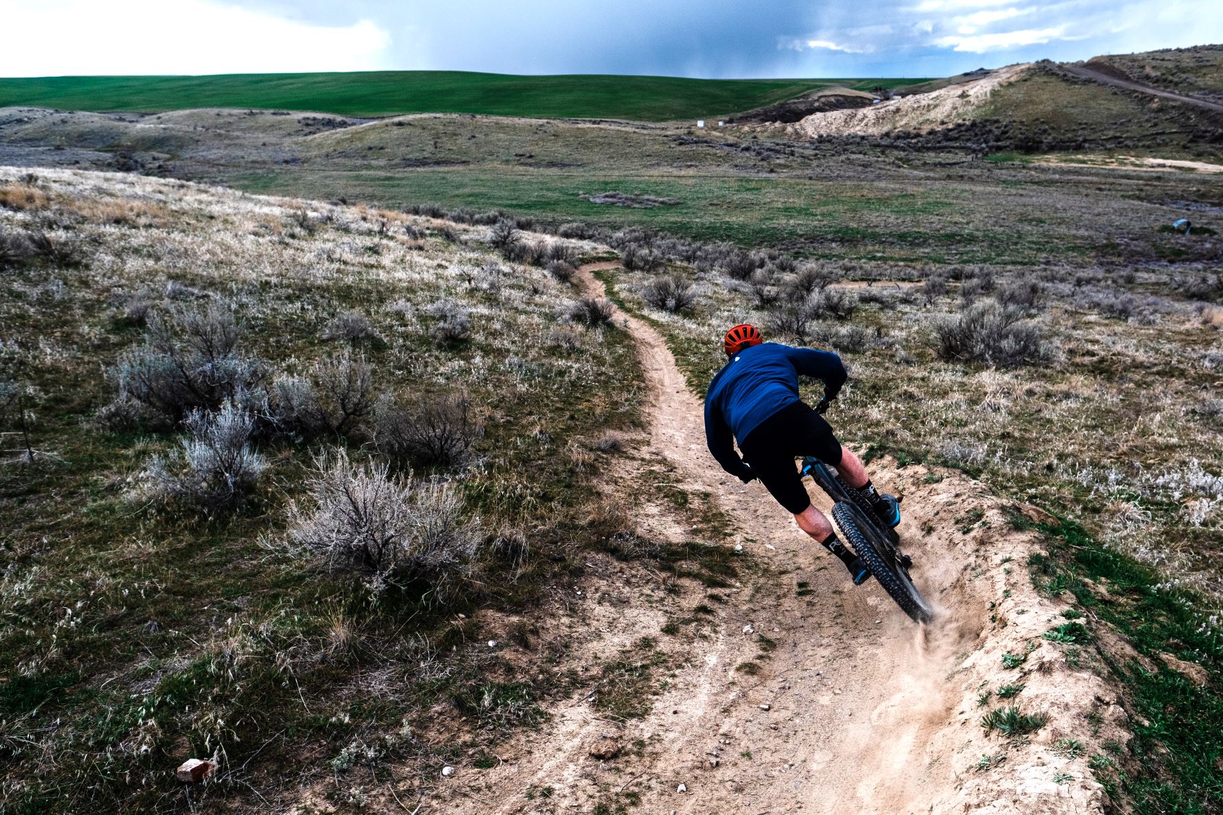 Mountain biker rounding a corner on a dirt singletrack through the rugged landscape of eastern Oregon.