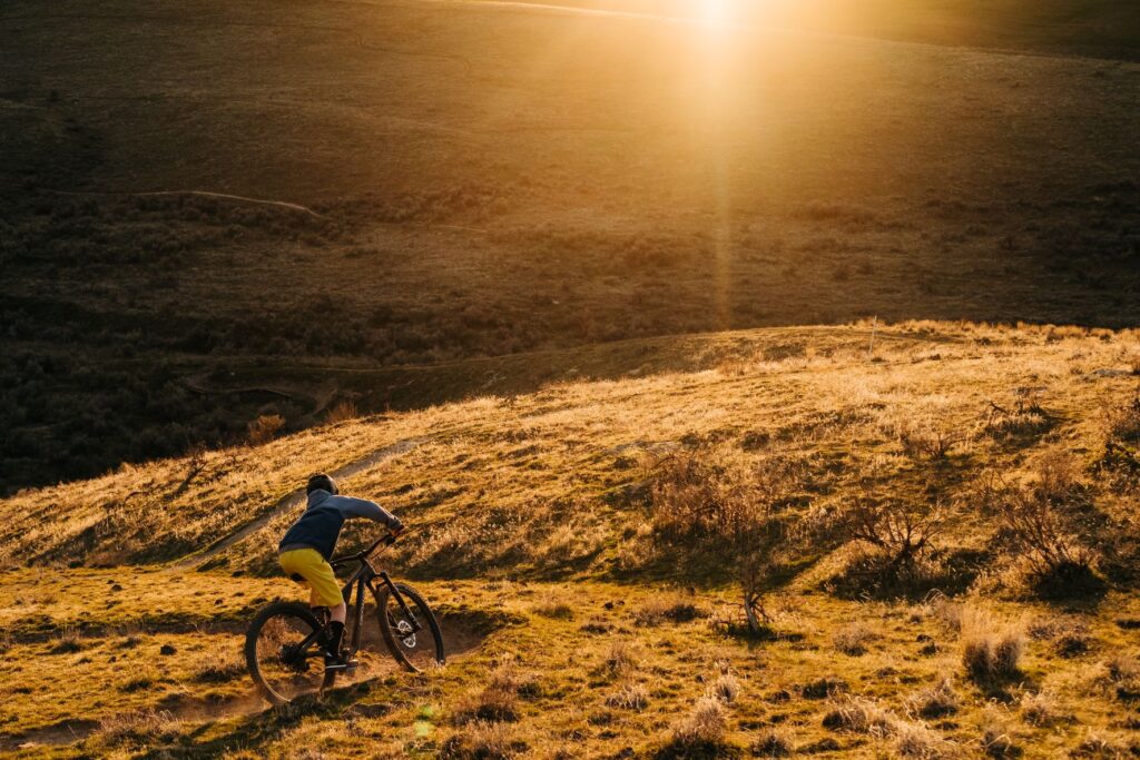 Mountain biker along a singletrack in in Echo, Oregon., along a brown dirt, rugged desert landcape, with sunset in the distance.