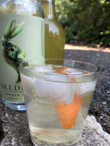 Peter Rabbit mocktail features clear spirit in a glass with ice, garnished with a carrot shaving.from non-alcoholic, pop-up Steady Bar in Coeur d'Alene, Idaho, is made with Seedlip,