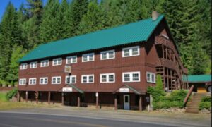 Three story Bear Creek Lodge and brown siding, white-framed windows, green slanted roof, and brick chimney.