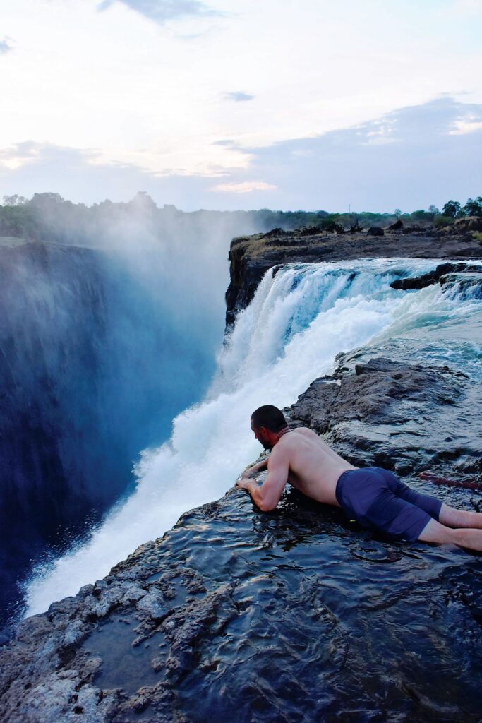 Steve Bailey belly down on rocks looking over the edge of Victoria Falls.