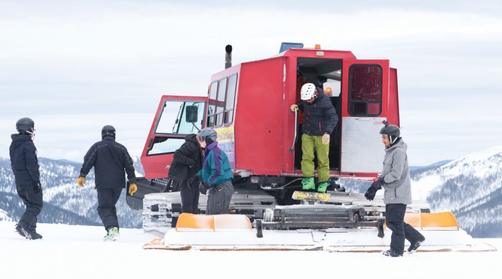 Red-colored snowcat -- an enclosed-cab, truck-sized, fully tracked vehicle designed to move on snow -- sits atop Eagle Peak to unload skiers.