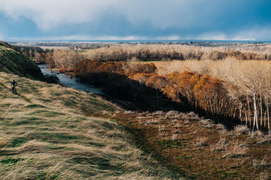 Brown, dry rugged desert landscape of eastern Oregon, and a single track mountain bike trails., with a biker cruising along.