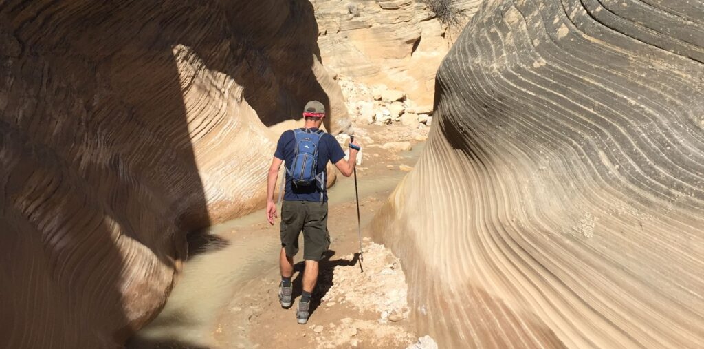 Man hiking through a slot canyon, comprised of sandstone.