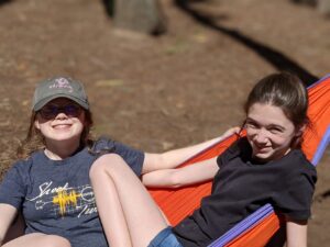 Two young teenage girls smiling at the camera while lounging in an ENO hammock in the sunshine.