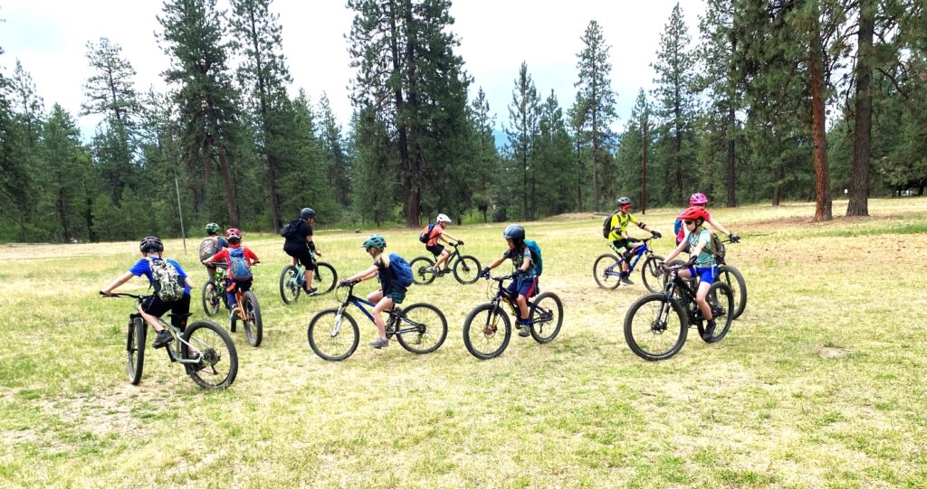 Youth mountain bike campers practicing riding techniques while riding in a circle over dirt and grass.