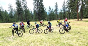Youth mountain bike campers practicing riding techniques while riding in a circle over dirt and grass.