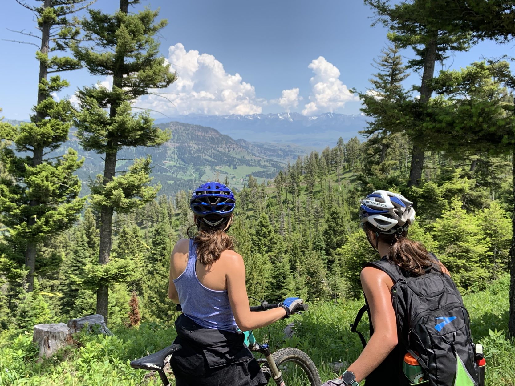 Two female mountain bike riders taking a break off their bikes to enjoy the distant view of mountains and forests across a valley near the Continental Divide Trail near Butte, Montana.