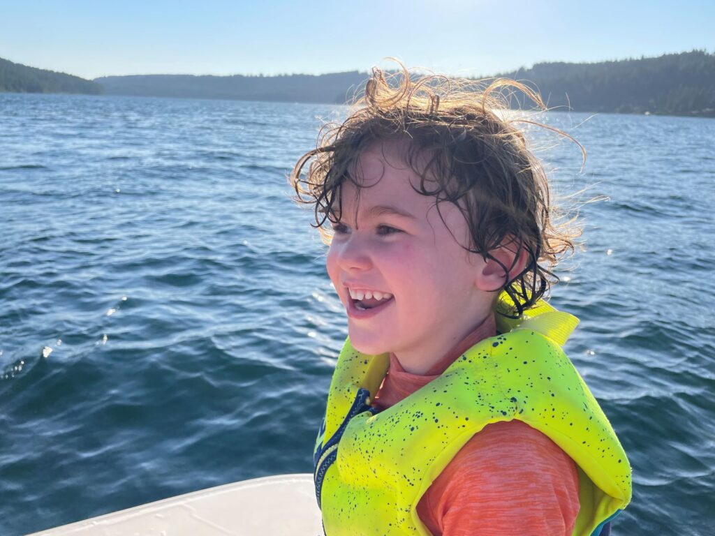 Smiling child wearing a neon yellow personal flotation device while swimming in a lake.