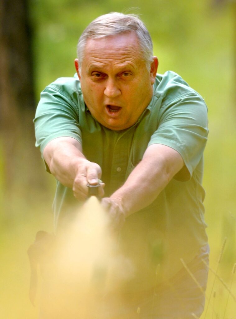 Chuck Bartlebaugh holding a can of bear spray with outstretched arms, with thumb pressing on top of spray can, demonstrating how to deploy bear repellent spray during a training session.