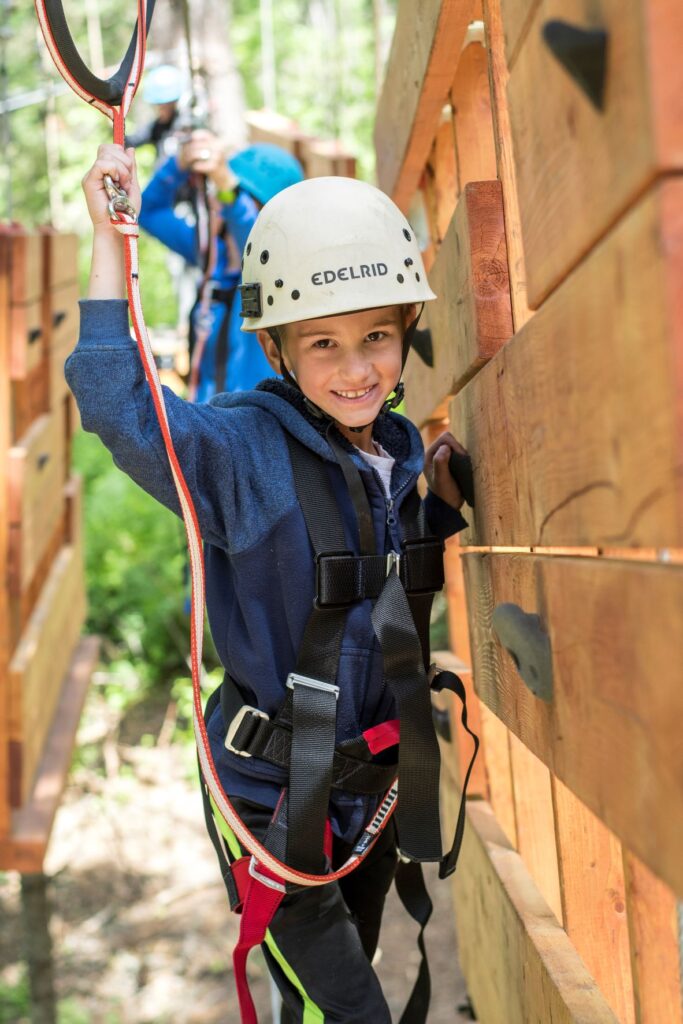 Child wearing a safety harness and helmet smiling at the camera while adventuring in the aerial park at Mica Moon. 