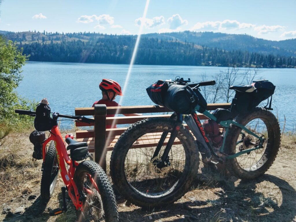 Child and parent taking a rest-break while biking on a trail above Fish Lake, with bikes resting against a bench.