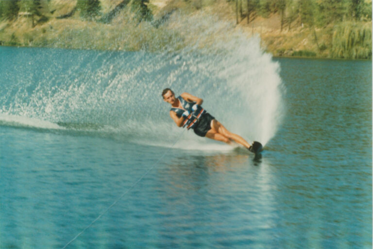 Man making a turn while water skiing on a lake, with a big spray of water coming from his ski.