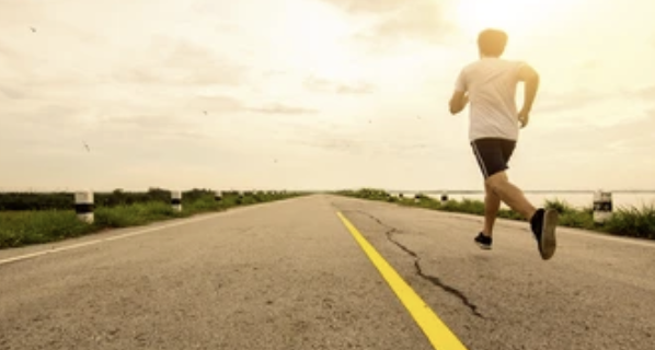 person running along an empty roadway with sunset colors on a flat horizon.