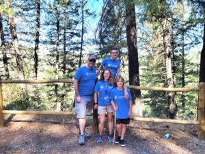 Volunteer on public lands: Livingston family on the Waikiki Springs Trail. Parents and children wearing matching blue t-shirts with forest trees in the background.