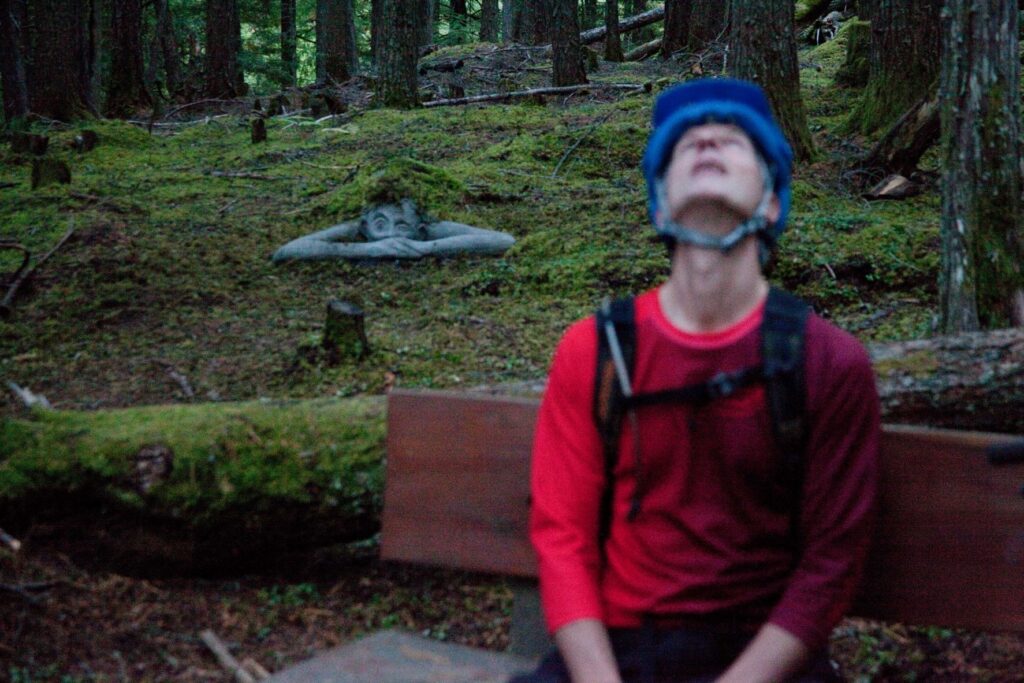 Writer Vince Hempsall takes a breather on the Kaslo River Trail, while mountain biking, with on of "The Koots" troll-like statues in the background.