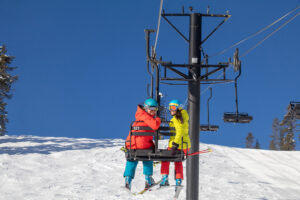 Two skiers riding a chairlift and looking back at the camera, smiling.