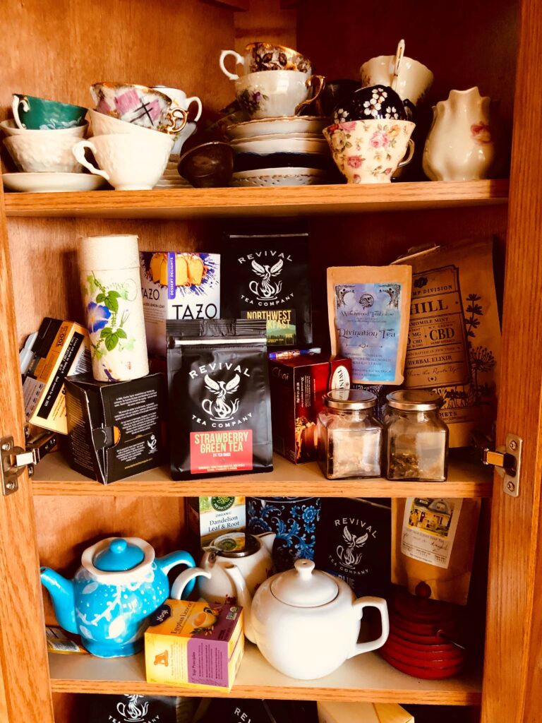 3 shelves full of stacks of tea cups, boxes of tea, and charming small tea pots