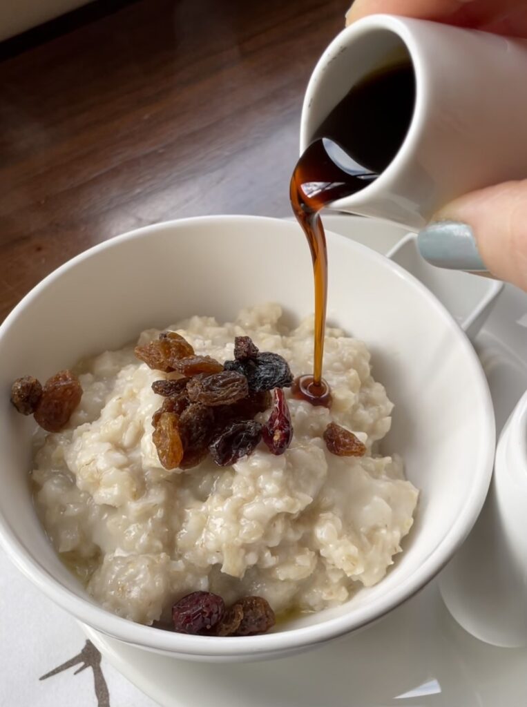 Dark maple syrup being poured over cooked oatmeal.