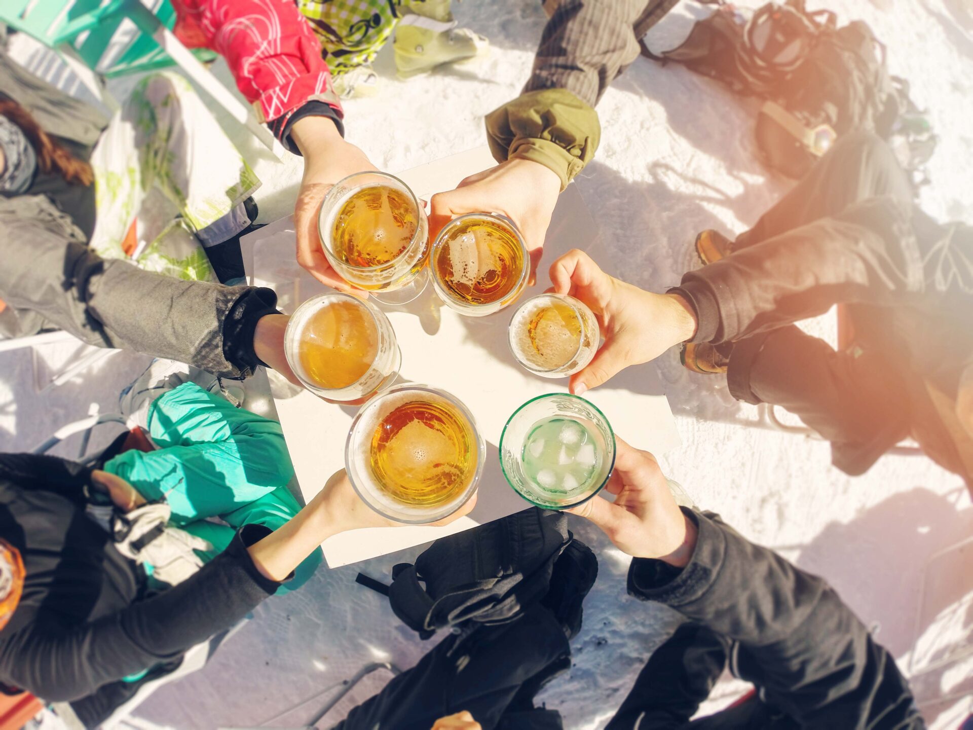 Above view of hands of five ski friends each holding a pint glass of beer in a circle on a table.