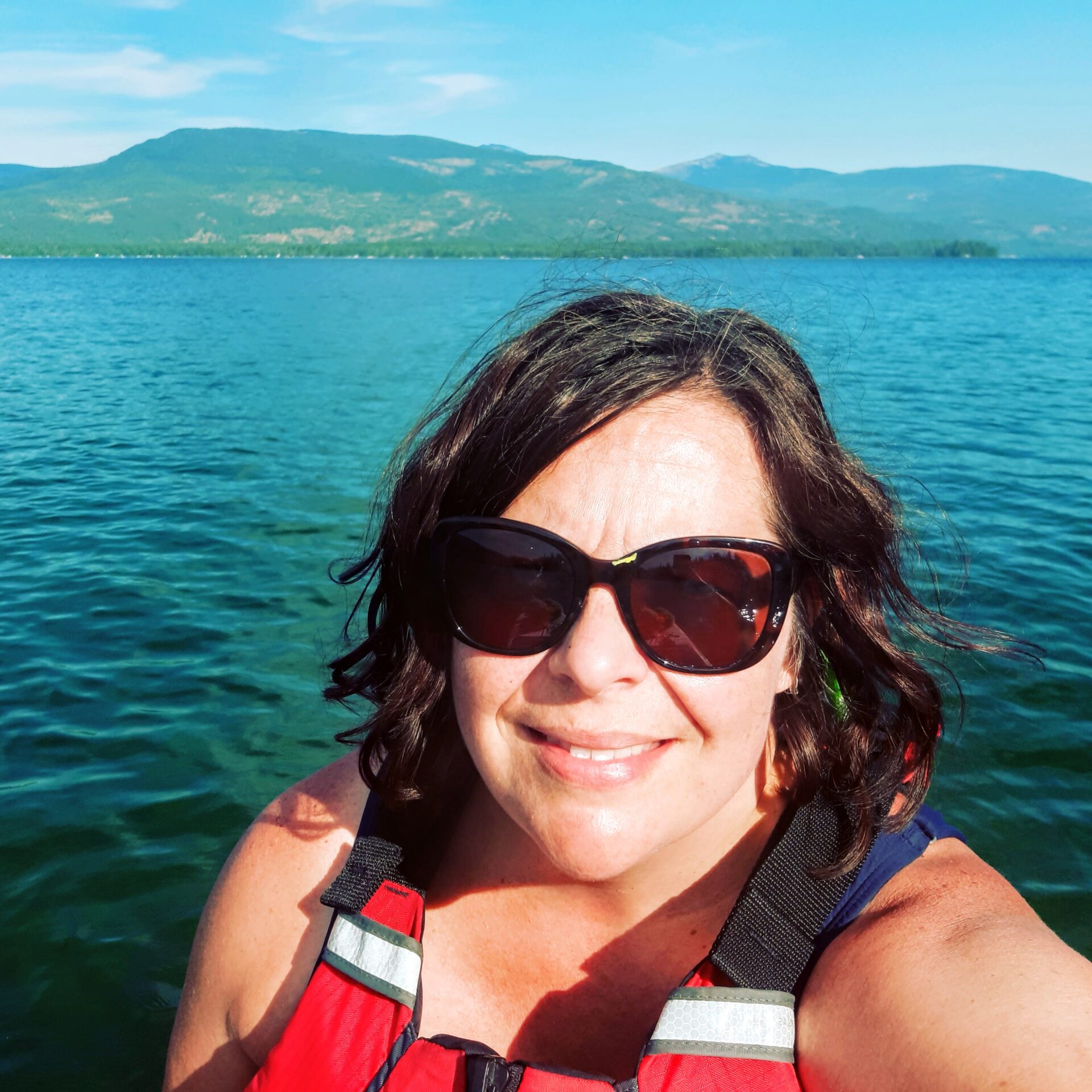 Amy paddling on Priest Lake -- wearing a red PFD with a background view of the lake and mountains.